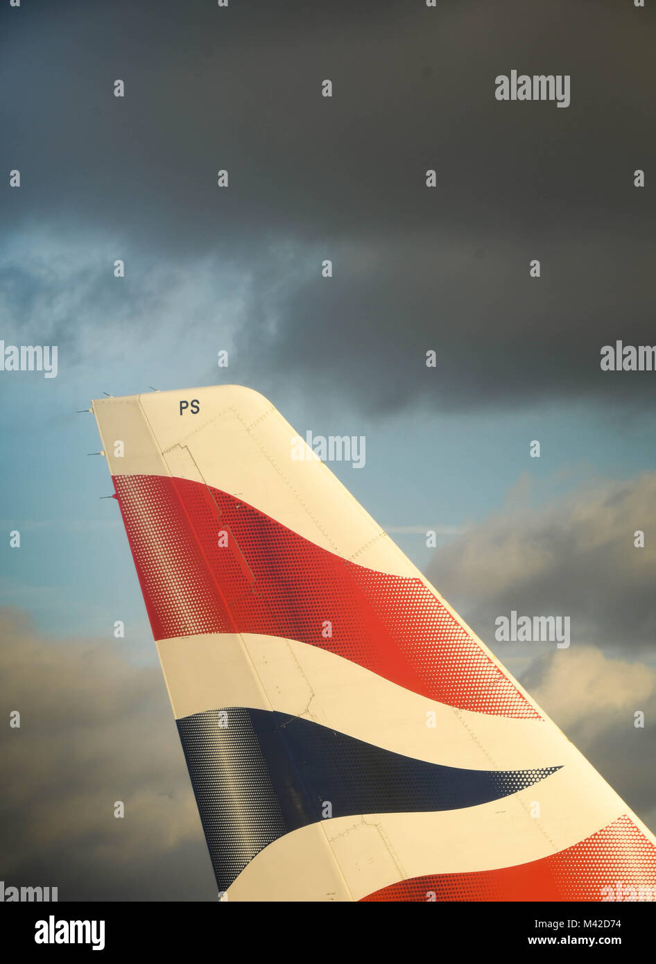 Close up del soleggiato pinna di coda di un British Airways Airbus A319 contro un cielo nuvoloso scuro Foto Stock