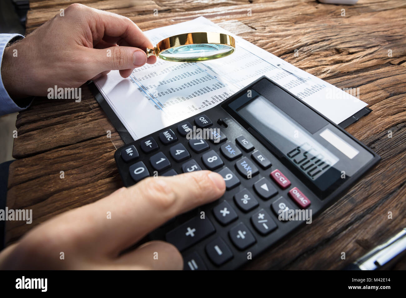 Imprenditore il mano che tiene la lente di ingrandimento mentre il calcolo rapporto finanziario con la calcolatrice Foto Stock