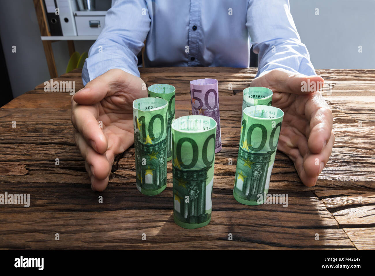 Close-up di un imprenditore la mano proteggere l'arrotolato moneta note sulla scrivania in legno Foto Stock