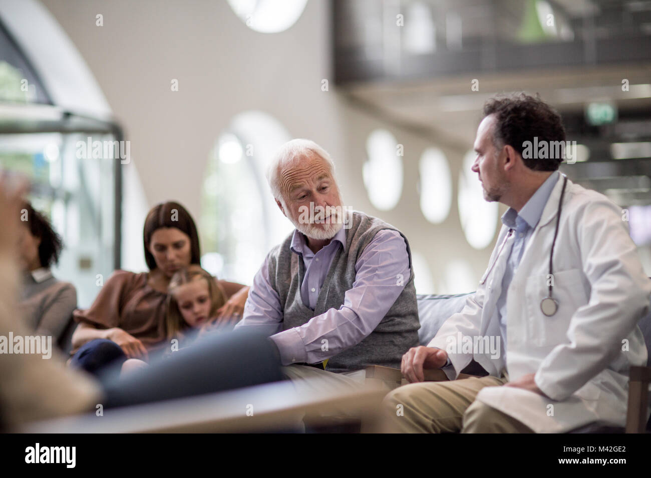 Maschio senior a parlare con il medico in un affollato ospedale sala di attesa Foto Stock