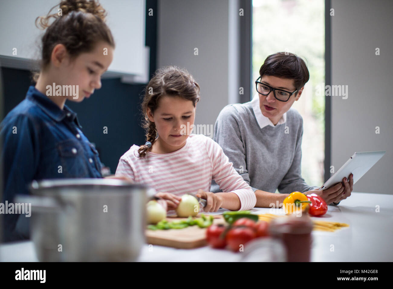 Mamma insegnamento figlie una ricetta utilizzando una tavoletta digitale Foto Stock