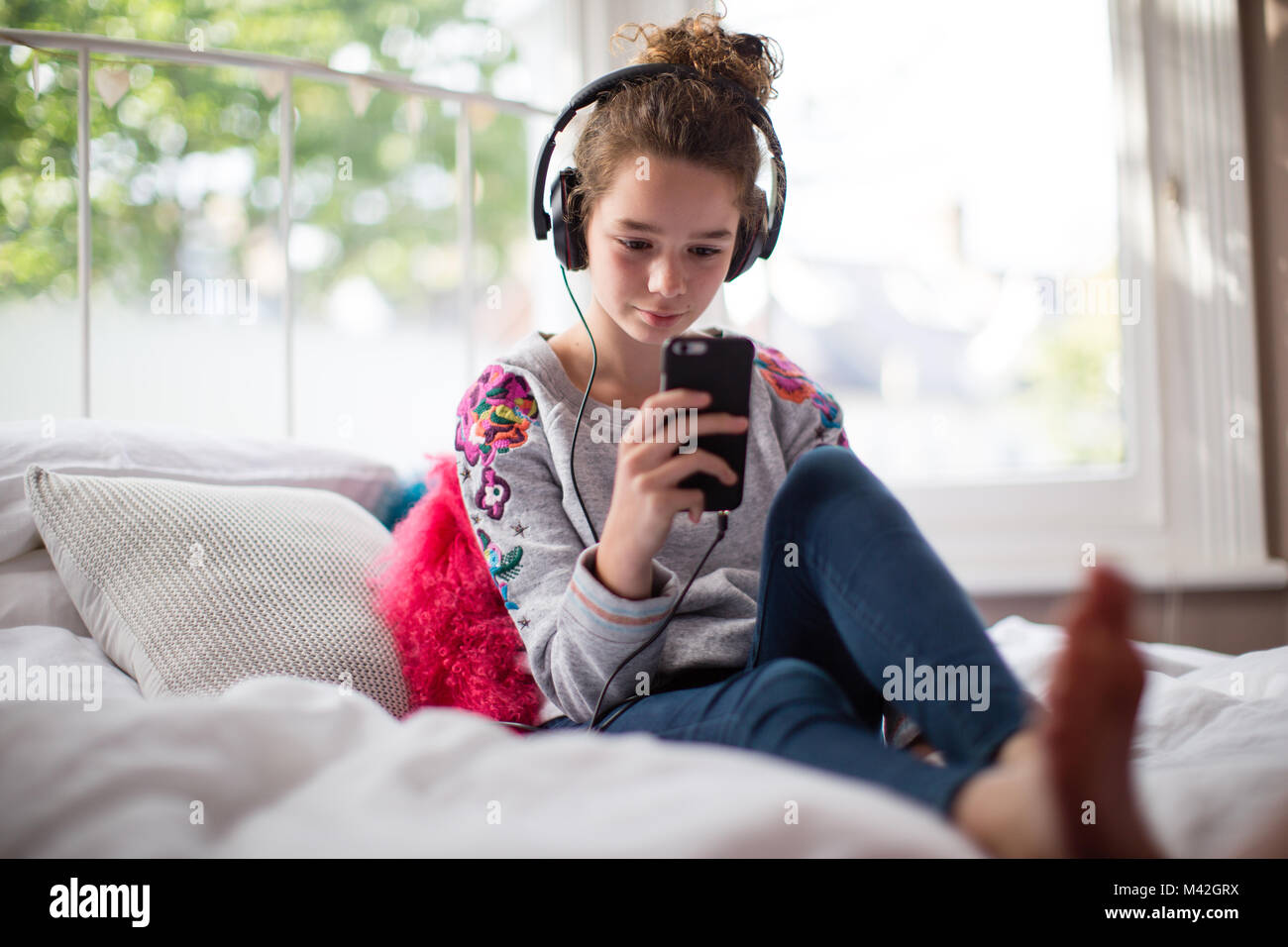 Adolescente in camera da letto ascoltando la musica sullo smartphone Foto Stock