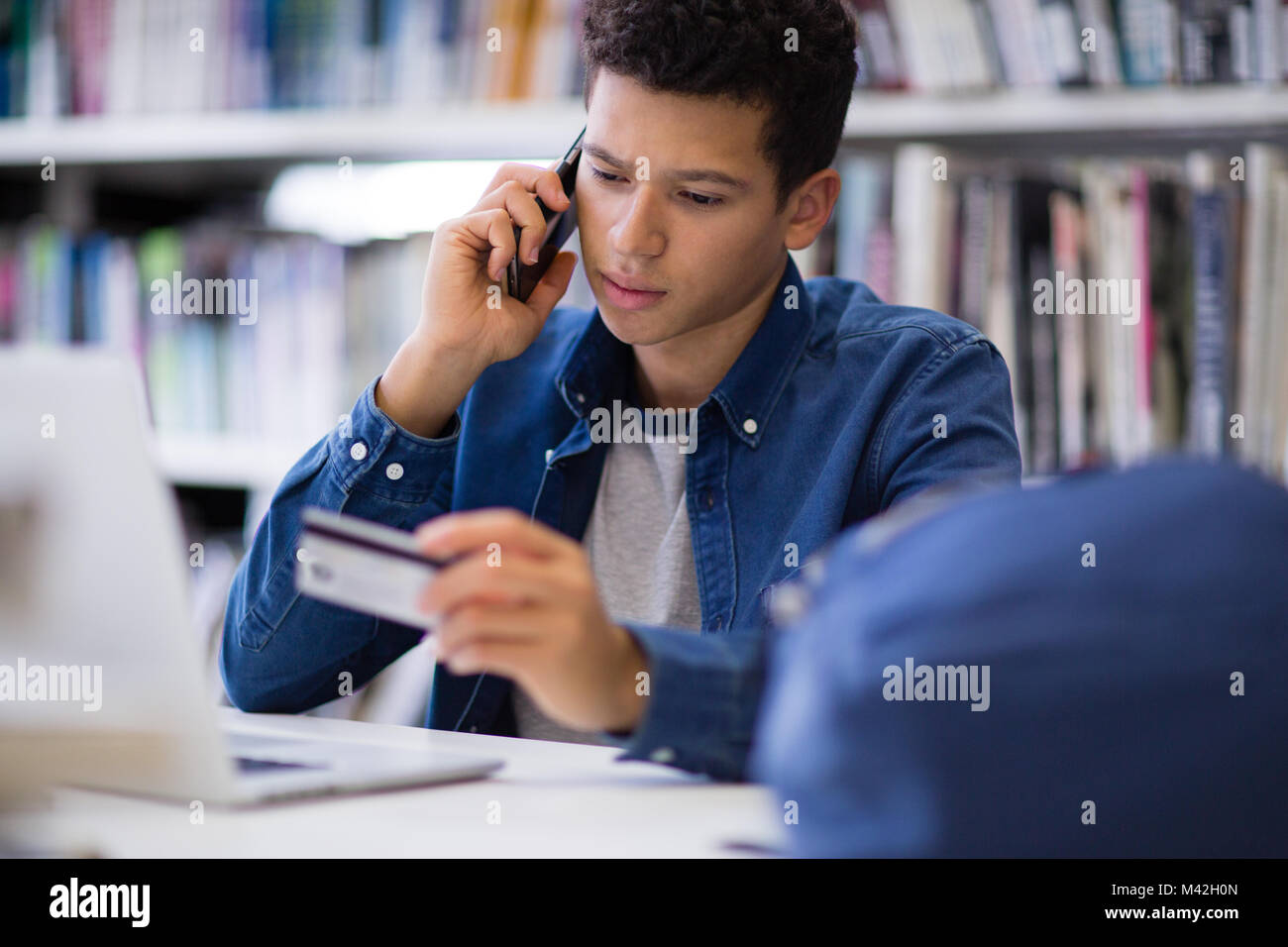 Studente su telefono cellulare con carta di credito Foto Stock
