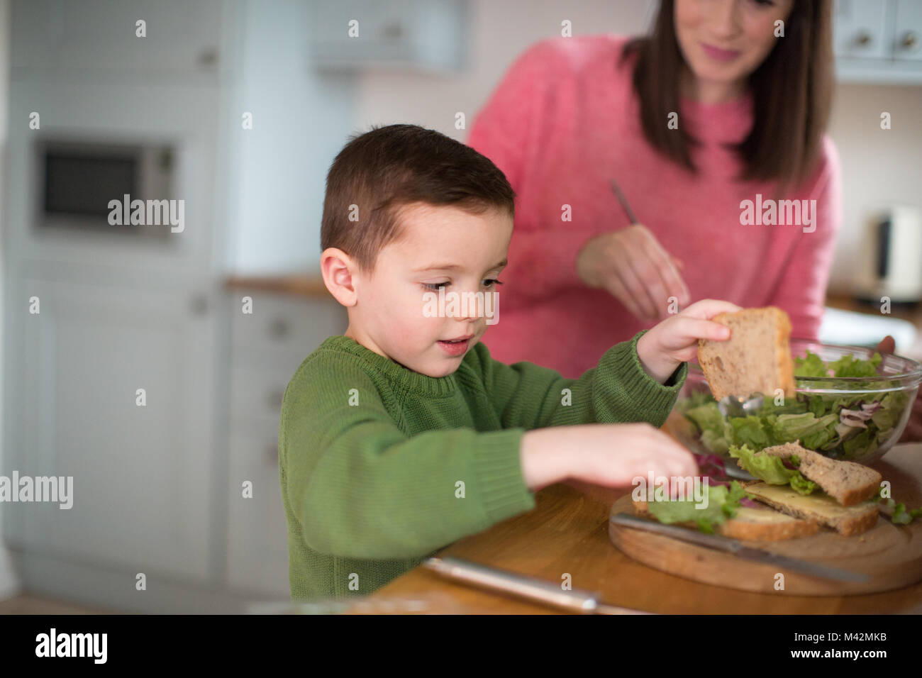Ragazzo facendo un sandwich con la madre aiutare Foto Stock