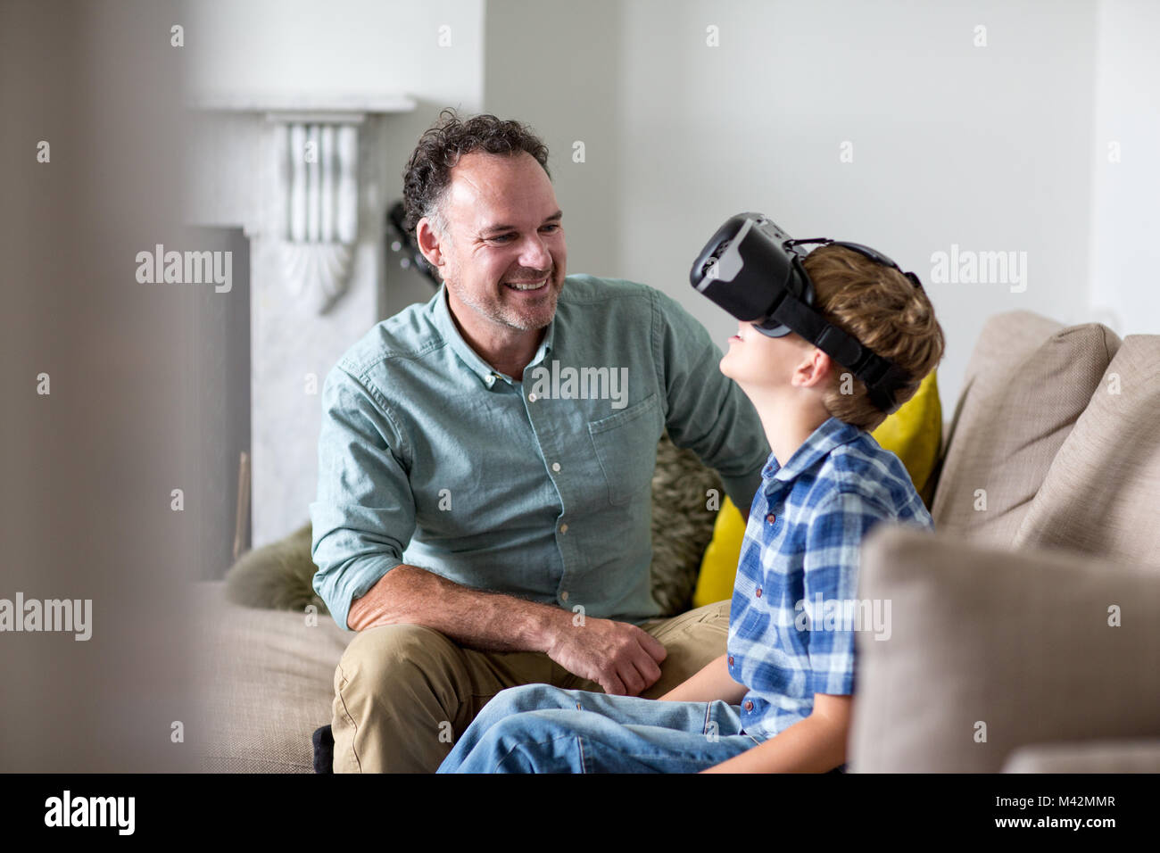 Boy utilizzando un auricolare VR gioco a casa con il Padre Foto Stock