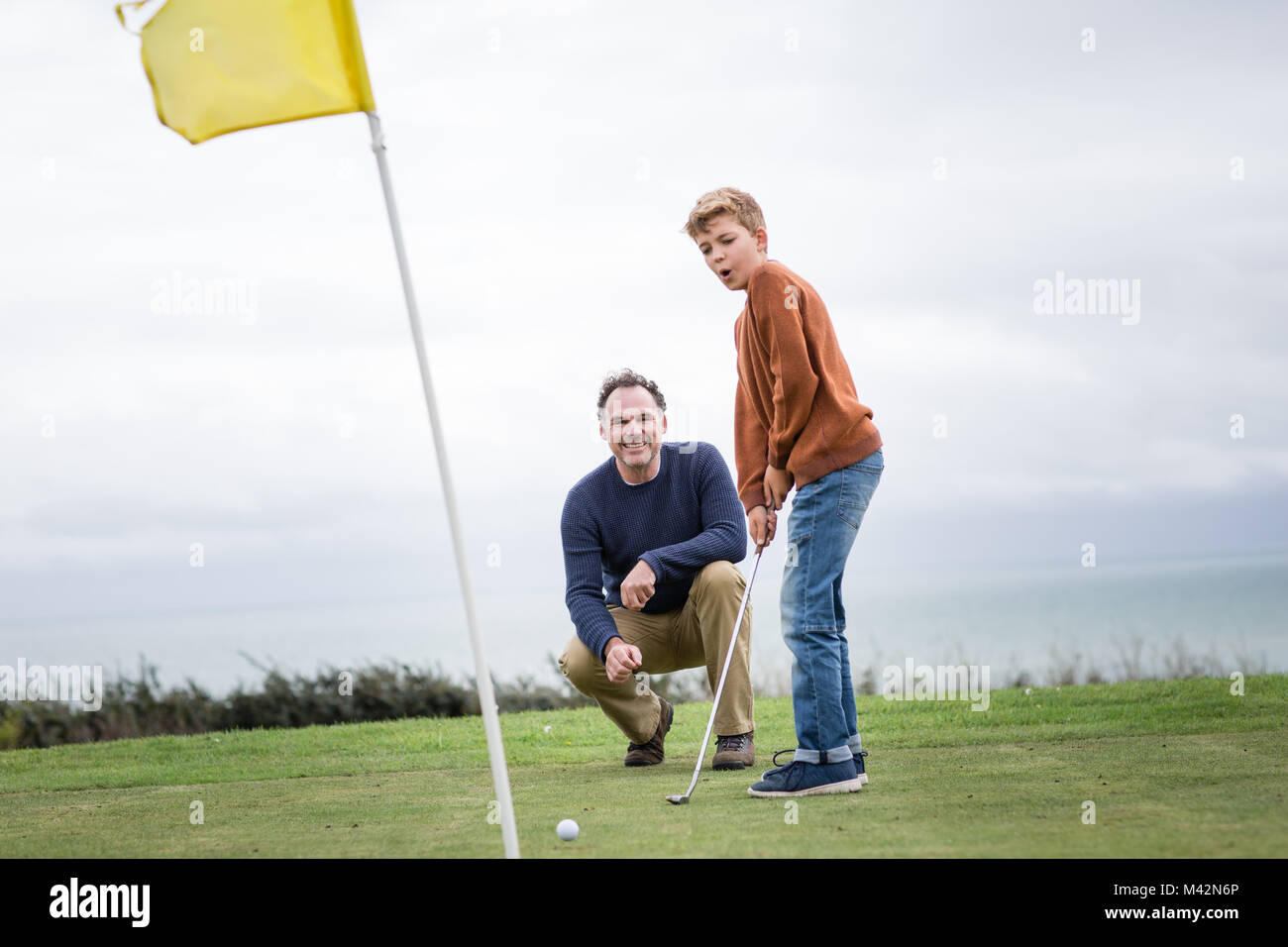 Padre guardando figlio giocare a golf Foto Stock