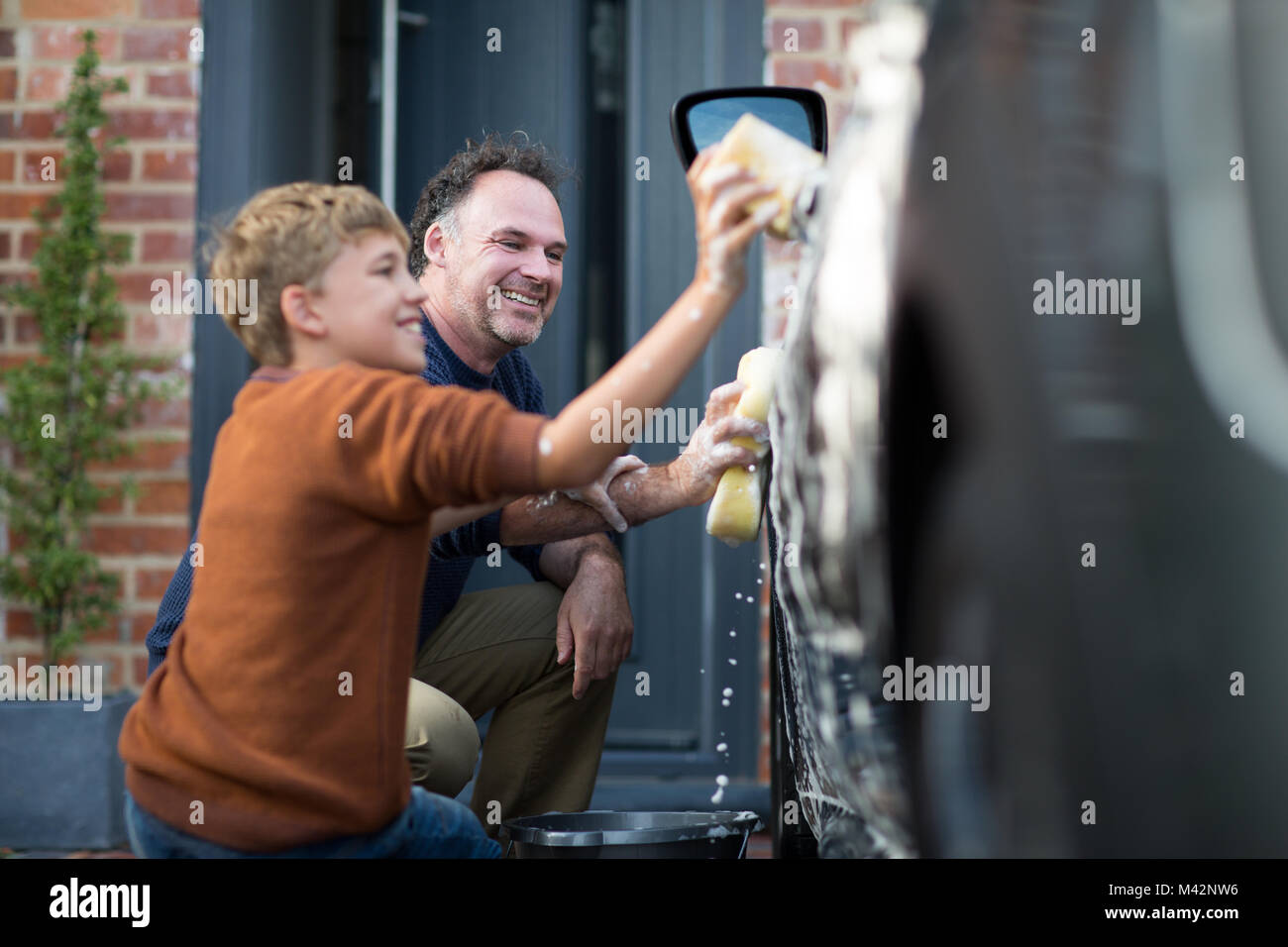 Figlio aiutando padre lavare la macchina Foto Stock