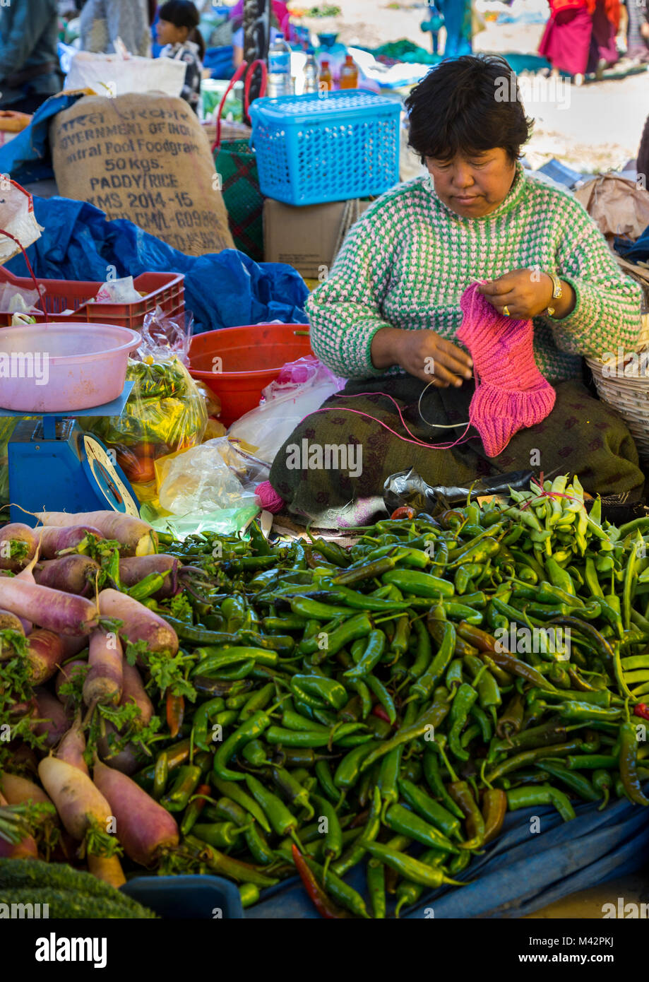 Punakha, Bhutan. Mercato di frutta e verdura, Donna vendita Chilis verde e rape facendo il suo lavoro a maglia. Foto Stock