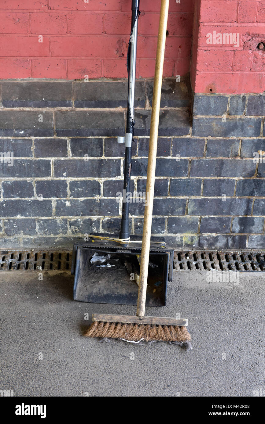 Una paletta e spazzola appoggiata contro il muro su una stazione piattaforma usata per spazzare fino la lettiera e mantenendo le piattaforme ordinate. spazzamento e pulizia. Foto Stock