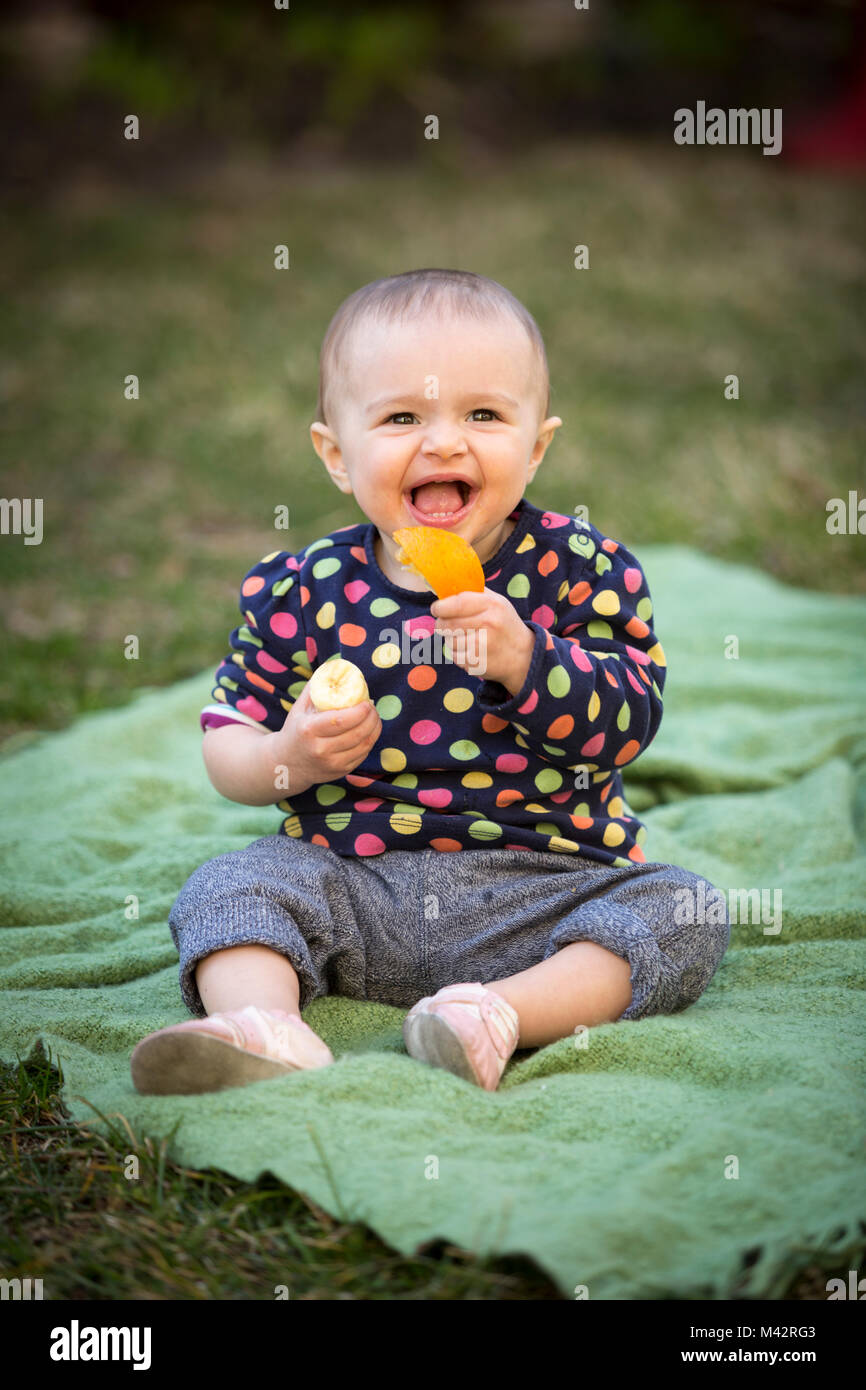 Un giovane toddle gode di una frutta snack di fettine di arancia e le banane in un cortile giardino. Foto Stock