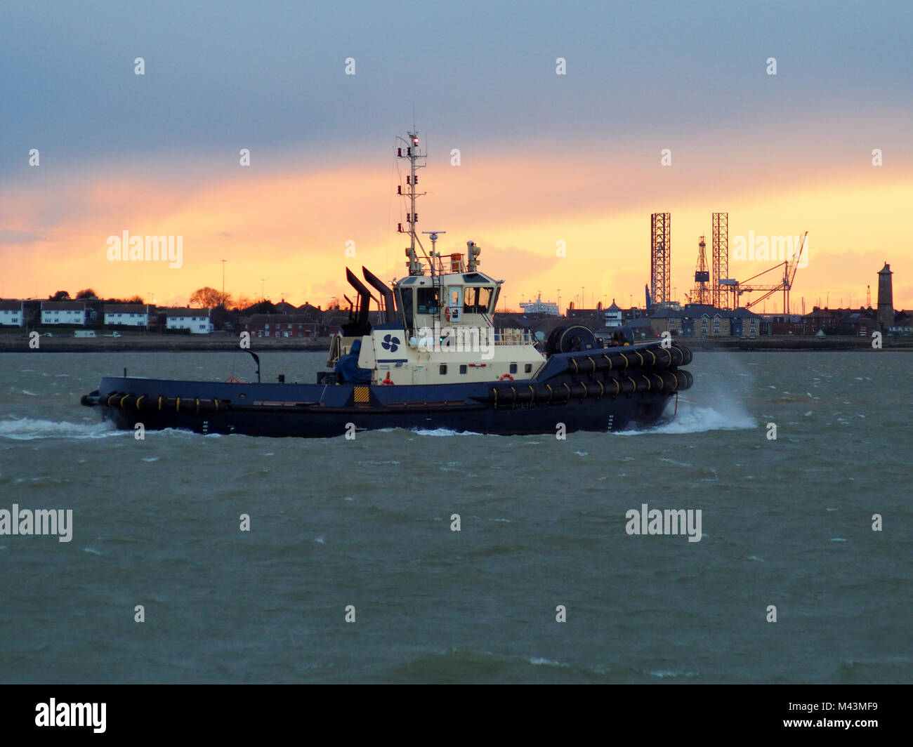 Harbour tug dal porto di Felixstowe fa il suo ritorno fino al fiume contro uno sfondo di colore arancione tramonto sul lungomare di Harwich, Suffolk, Regno Unito Foto Stock