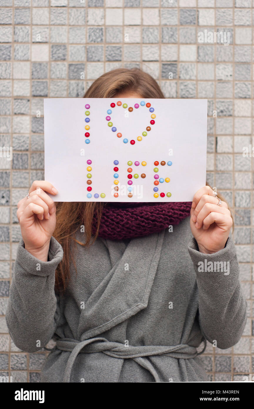 Giovane donna in possesso di una carta con le parole "I Love Life" nella parte anteriore del suo viso Foto Stock