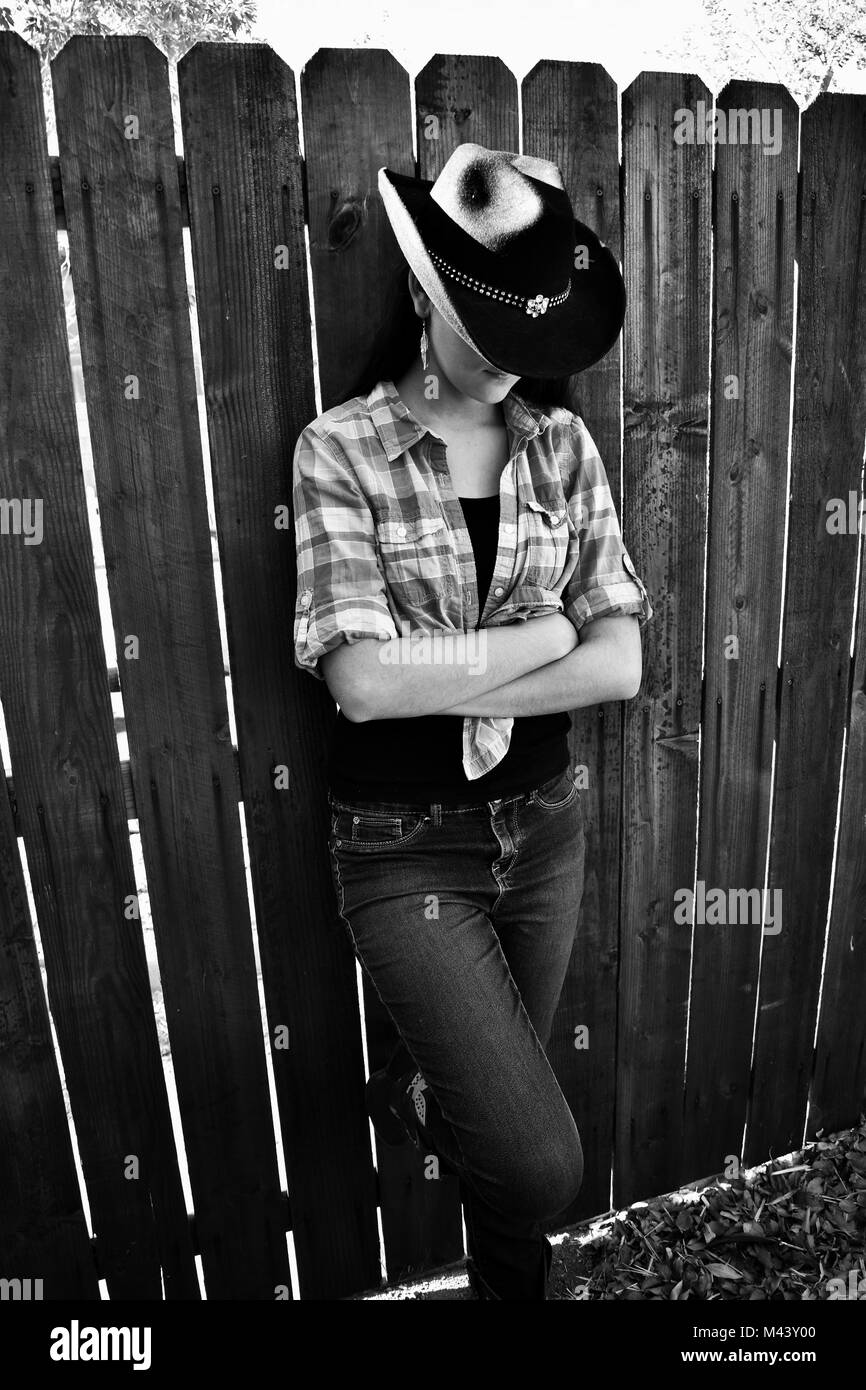 Bianco e Nero Cowgirl appoggiata contro una recinzione di legno Foto Stock