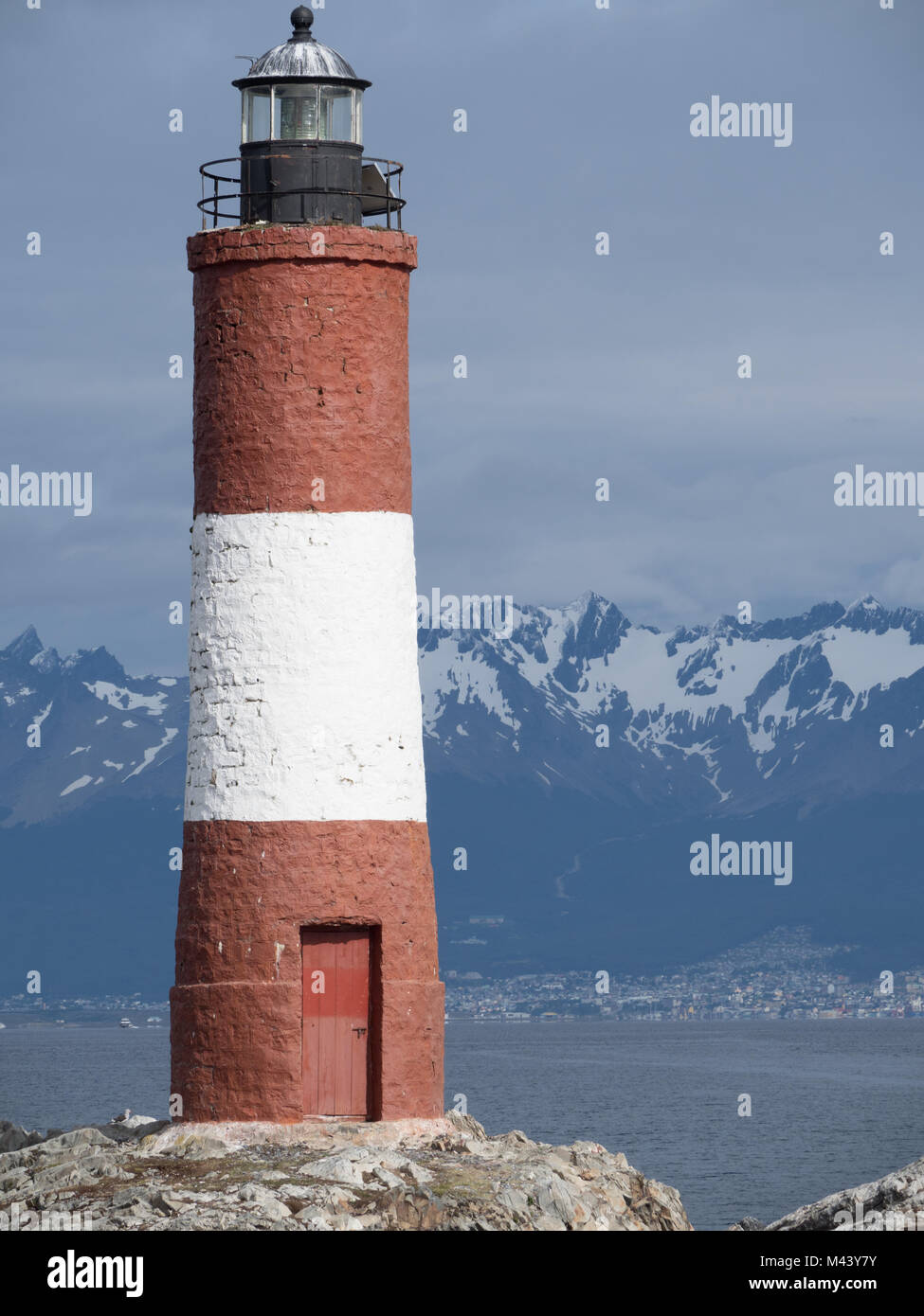 Un bianco e la ruggine faro sul Canale di Beagle. Un pannello solare visibile vicino alla luce e Ushuaia Argentina, montagne innevate e cielo nuvoloso ski Foto Stock