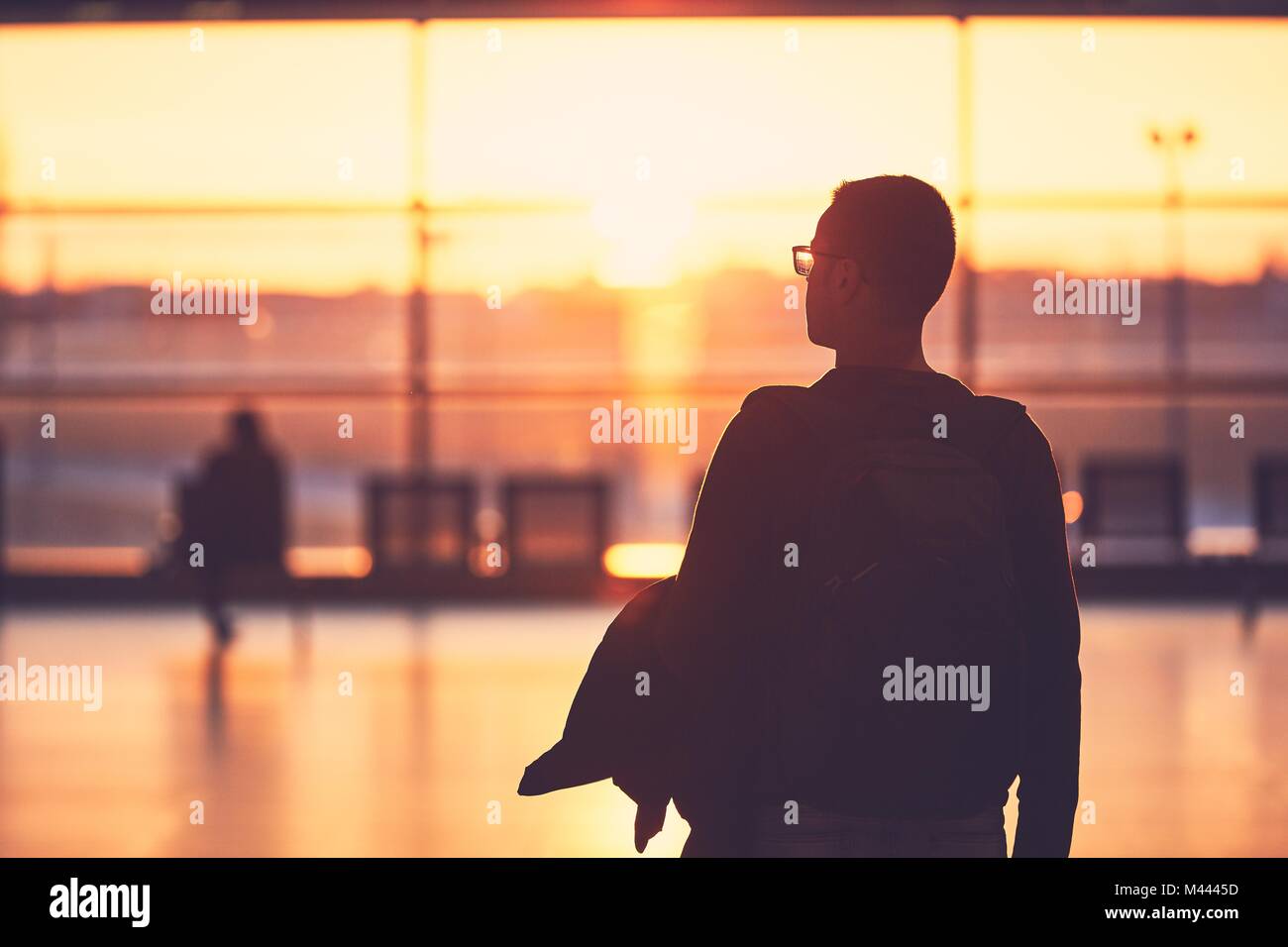 Silhouette del giovane uomo in aeroporto. Foglie di viaggiatori al gate durante il tramonto dorato. Foto Stock