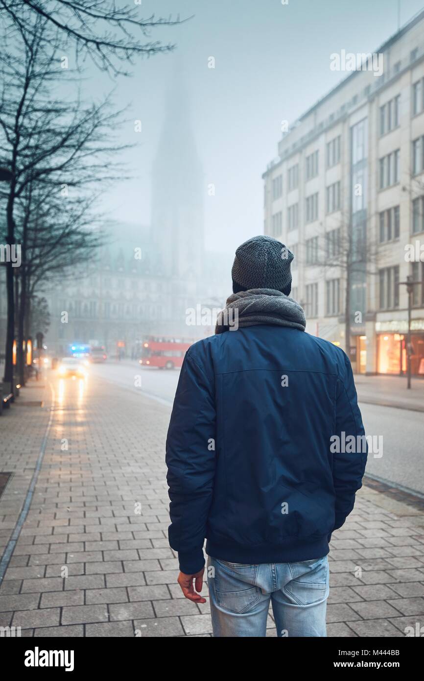 L'uomo sulla strada di città in cupo nebbioso giorno contro il traffico con rispondere il servizio di emergenza medica. Amburgo, Germania. Foto Stock