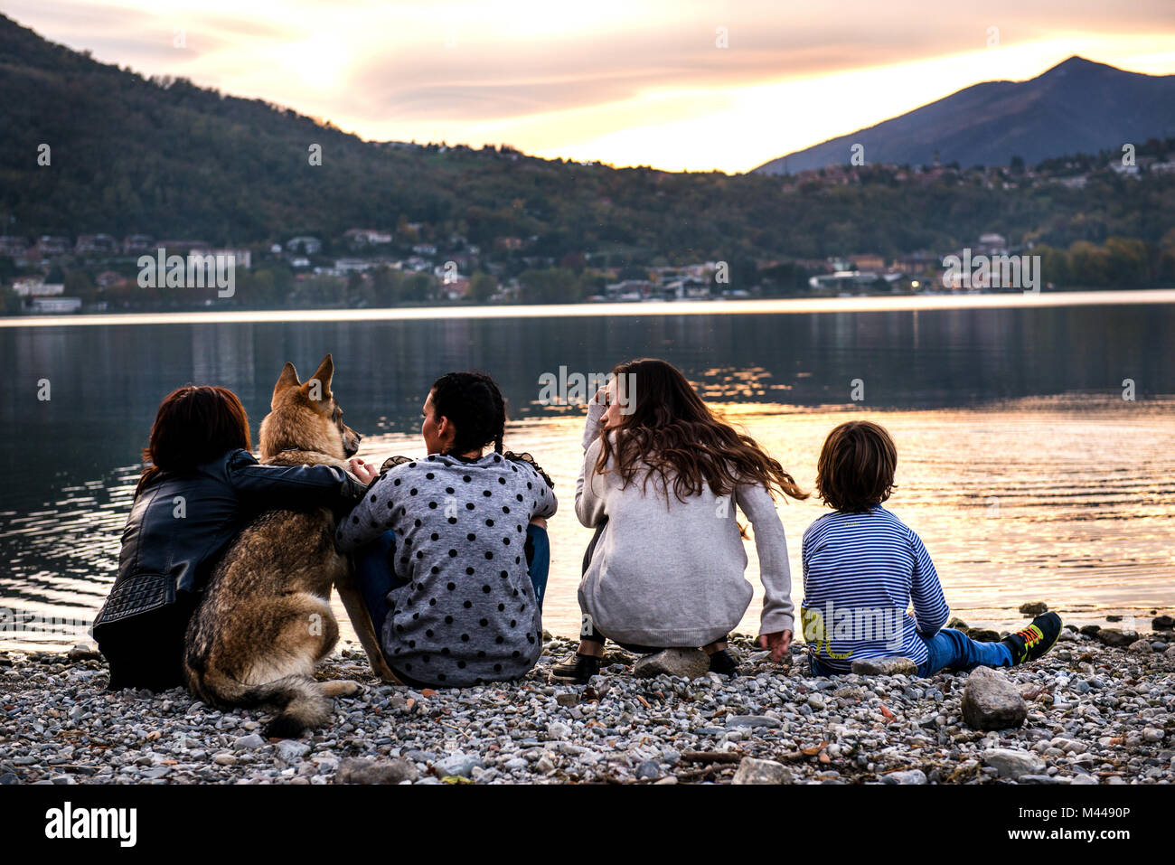 Vista posteriore del ragazzo con la famiglia e il cane dal fiume al tramonto, Vercurago, Lombardia, Italia Foto Stock