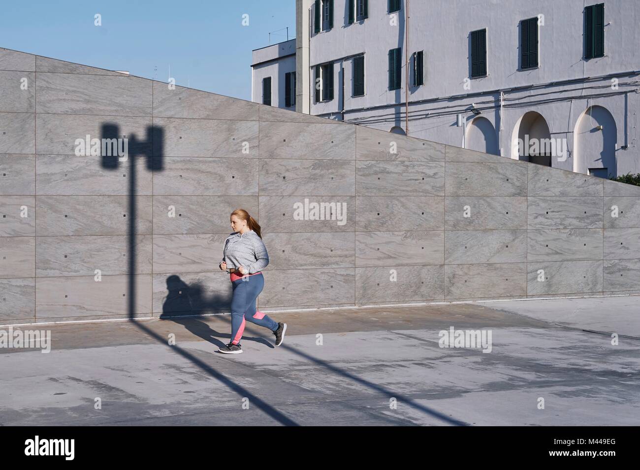 Sinuosa femmina giovane runner che corre lungo il marciapiede Foto Stock