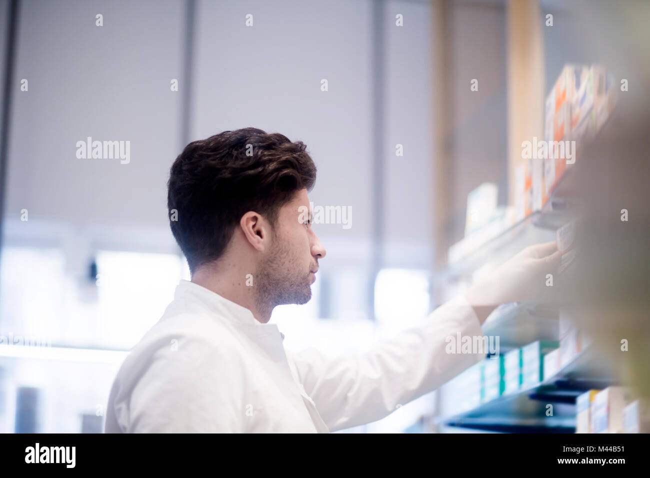 Giovane maschio il farmacista la rimozione di farmaco medicale da farmacia ripiani Foto Stock