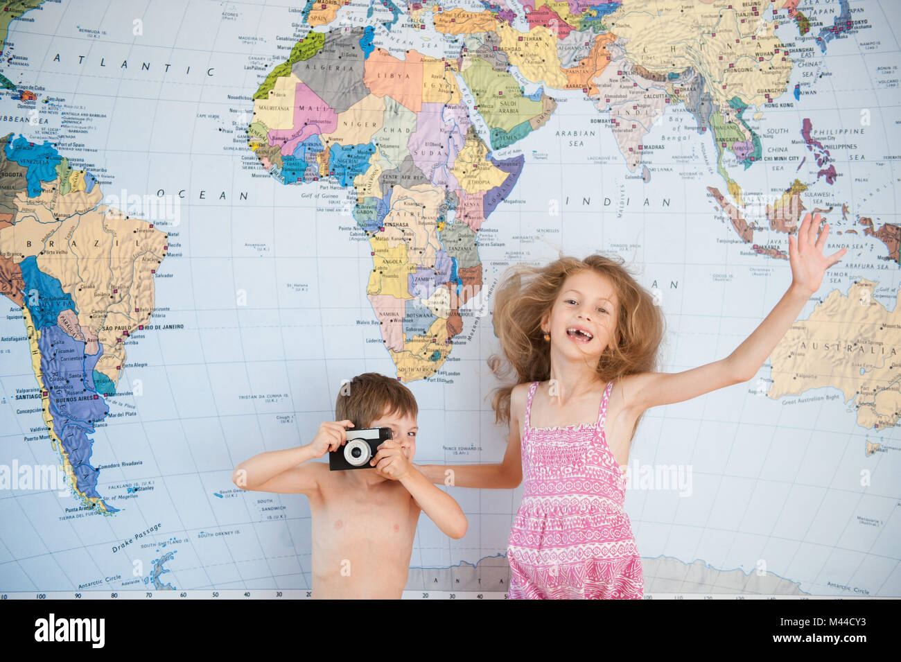 Ragazzino con fotocamera vintage e una ragazza in abito avendo divertimento sullo sfondo della mappa del mondo Foto Stock