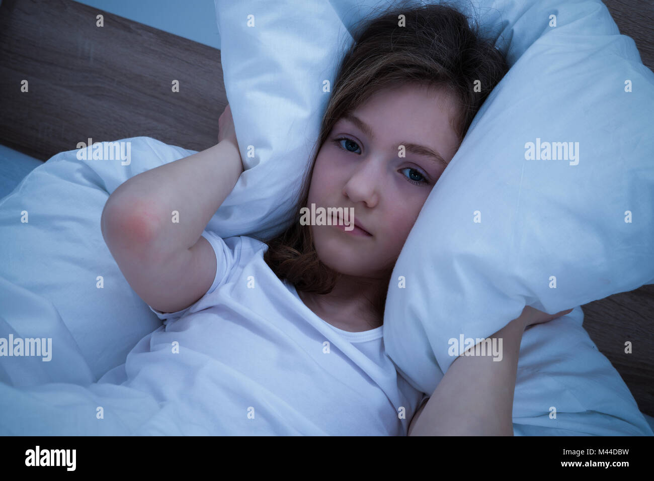 Carino ragazza distesa nel letto che soffrono di suono che copre le sue orecchie con cuscino Foto Stock