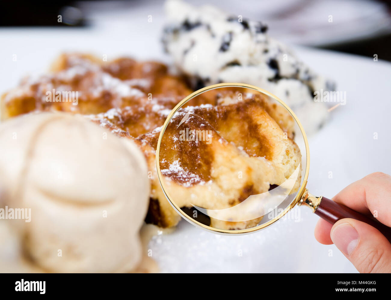 Primo piano della mano scrutare waffle servita nella piastra attraverso la lente di ingrandimento nel ristorante Foto Stock