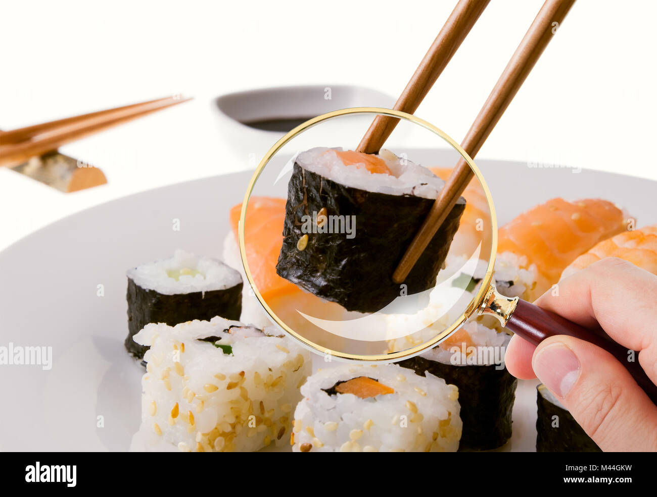 Primo piano della mano a scrutare il sushi servita nella piastra attraverso la lente di ingrandimento nel ristorante Foto Stock
