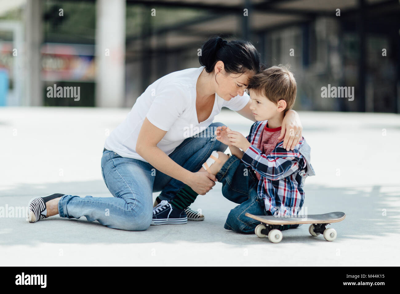 Ritratto di una madre che abbraccia il suo giovane skater boy con un ginocchio infortunato Foto Stock