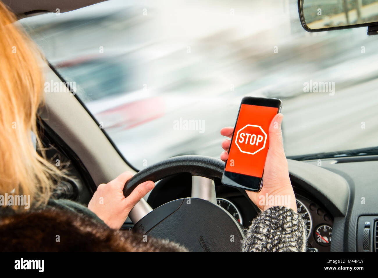 La donna possiede uno smartphone con segno di stop in sua mano durante la guida Foto Stock