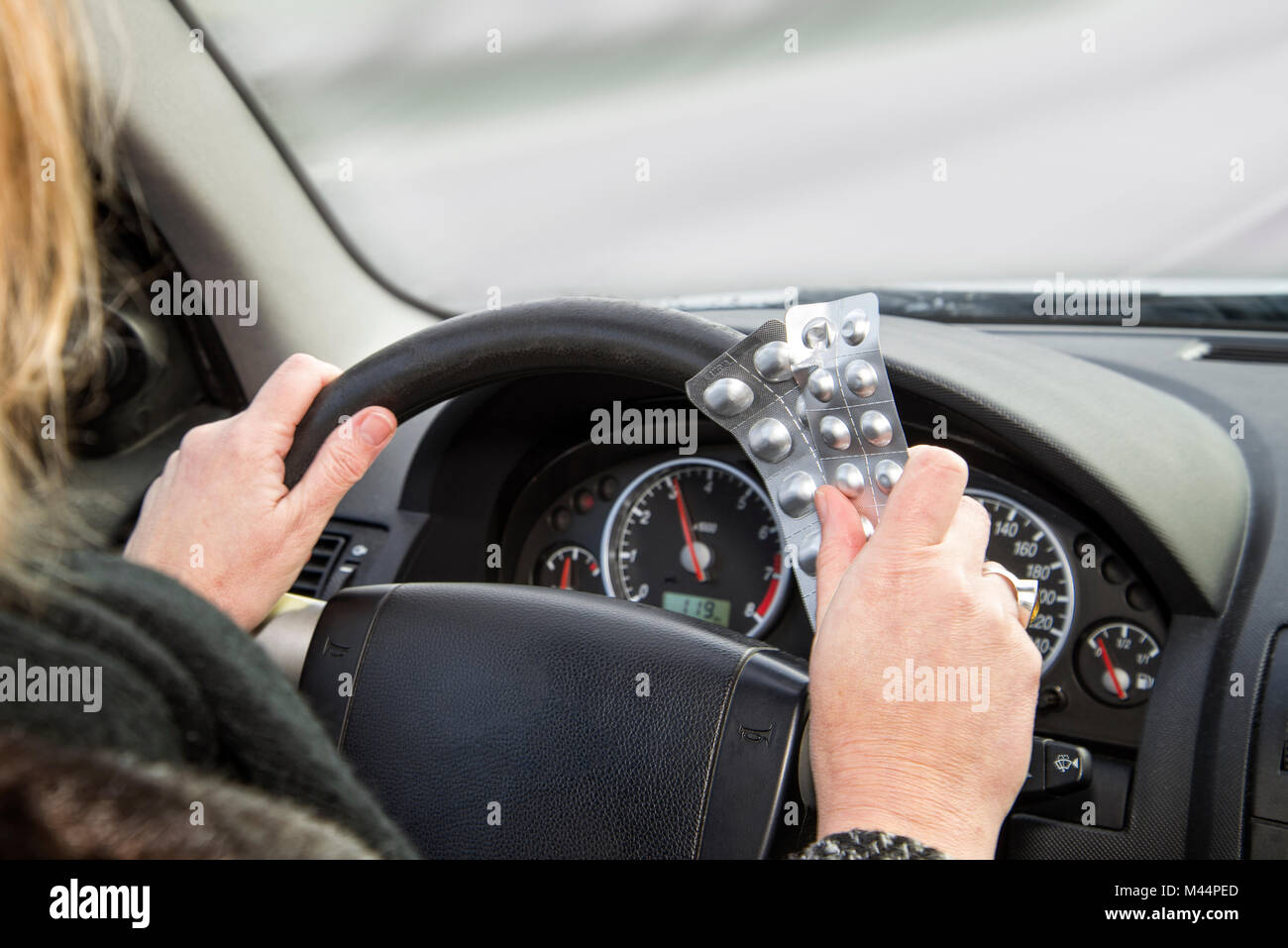 Mani con confezioni di compresse al volante di una vettura durante la guida Foto Stock