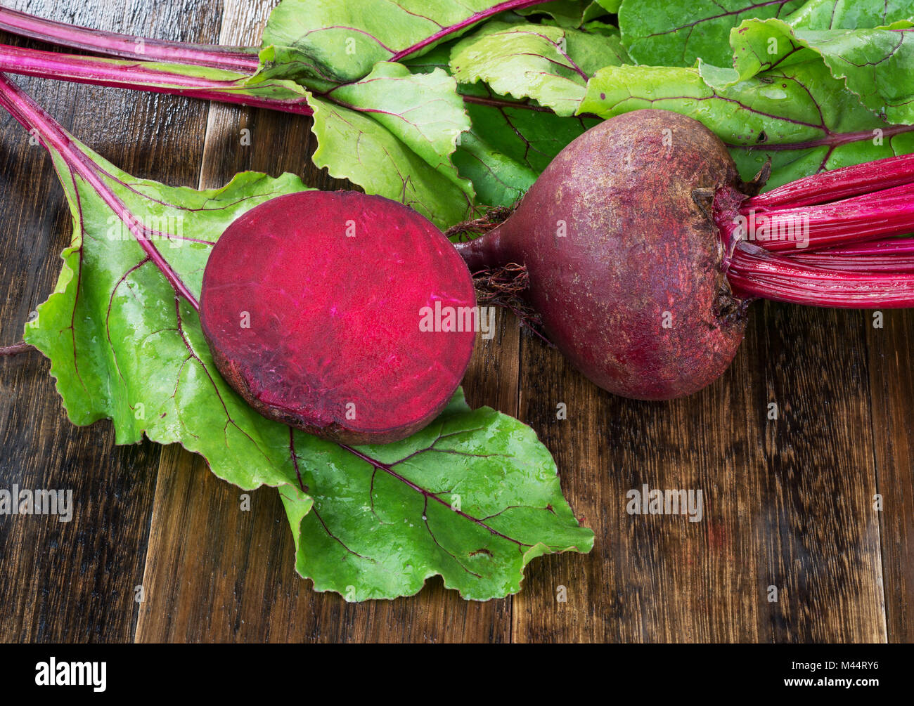 Barbabietole fresche con foglie sul bagnato rustico in legno tabella.Tutto e tagliare barbabietole Foto Stock