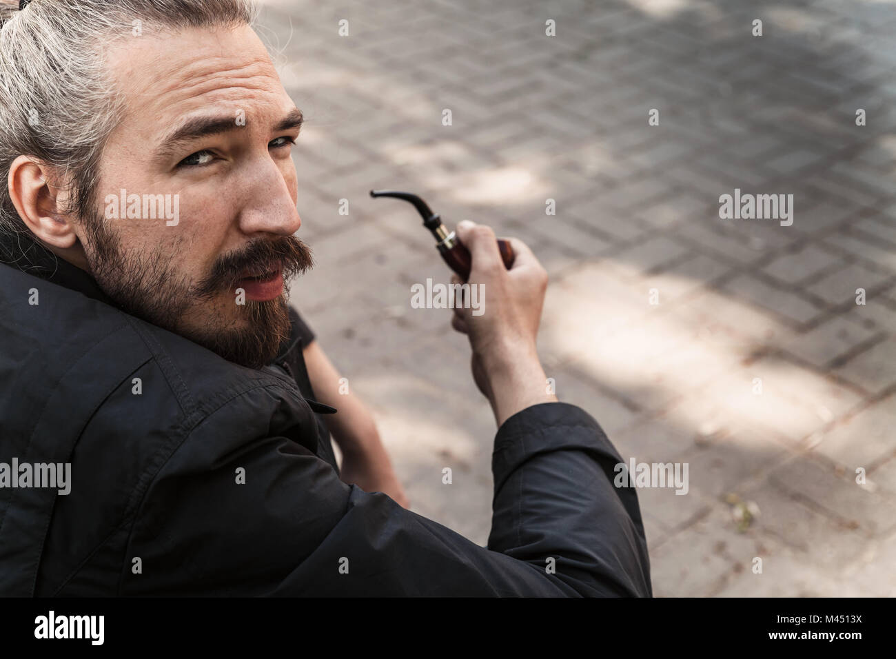 Grave giovane uomo barbuto condotto dei fumi, close-up ritratto all'aperto con il fuoco selettivo Foto Stock