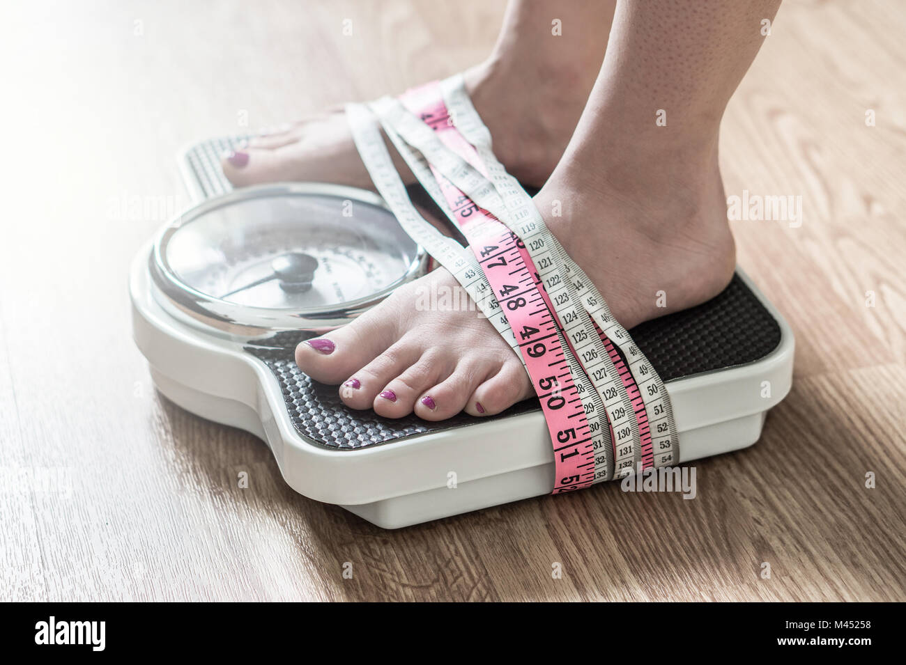 Anoressia e disturbo alimentare concetto. I piedi legati con nastro di misurazione a una scala di peso. Dipendenza e ossessione per la perdita di peso. Foto Stock