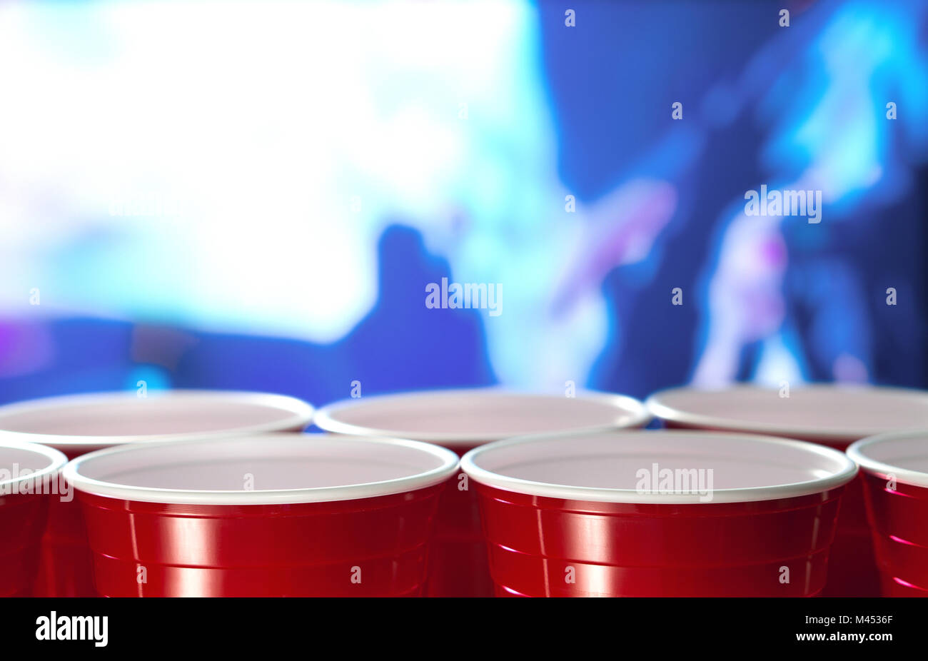 Rosso in plastica party tazze in una fila in una discoteca piena di gente a ballare sulla pista da ballo in background. Perfetto per la commercializzazione e la promozione. Foto Stock