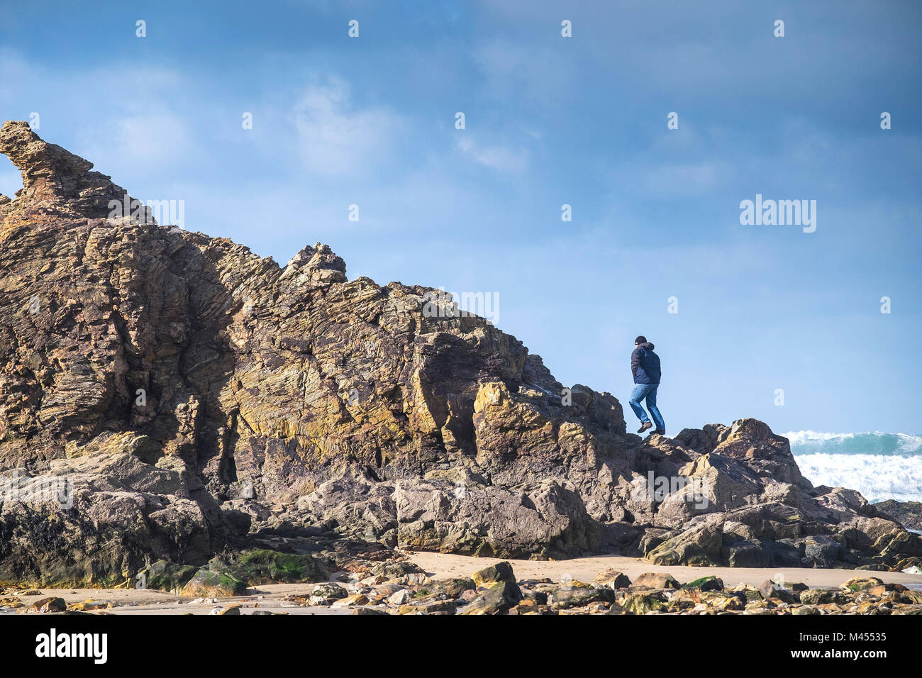 Un uomo di arrampicata su roccia della cappella sulla spiaggia a Perranporth in Cornwall Regno Unito. Foto Stock