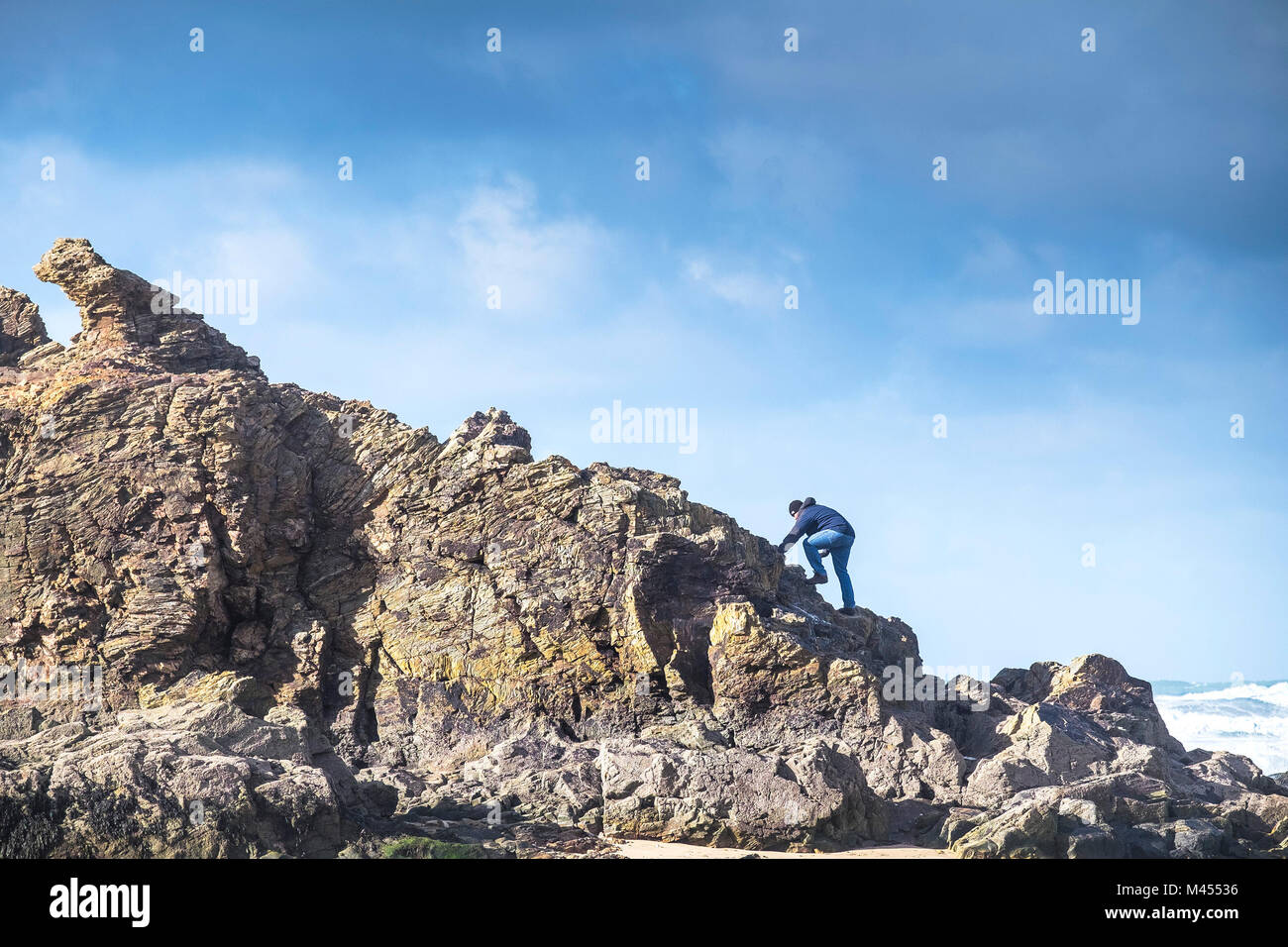 Un uomo di arrampicata su roccia della cappella sulla spiaggia a Perranporth in Cornwall Regno Unito. Foto Stock