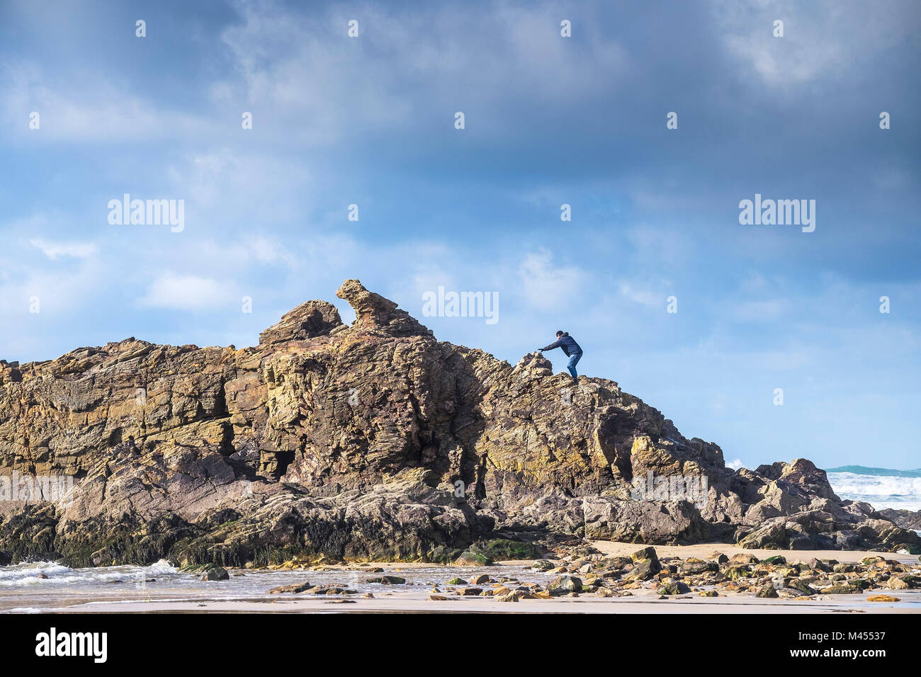 Un uomo di arrampicata su roccia della cappella sulla spiaggia a Perranporth in Cornwall Regno Unito. Foto Stock