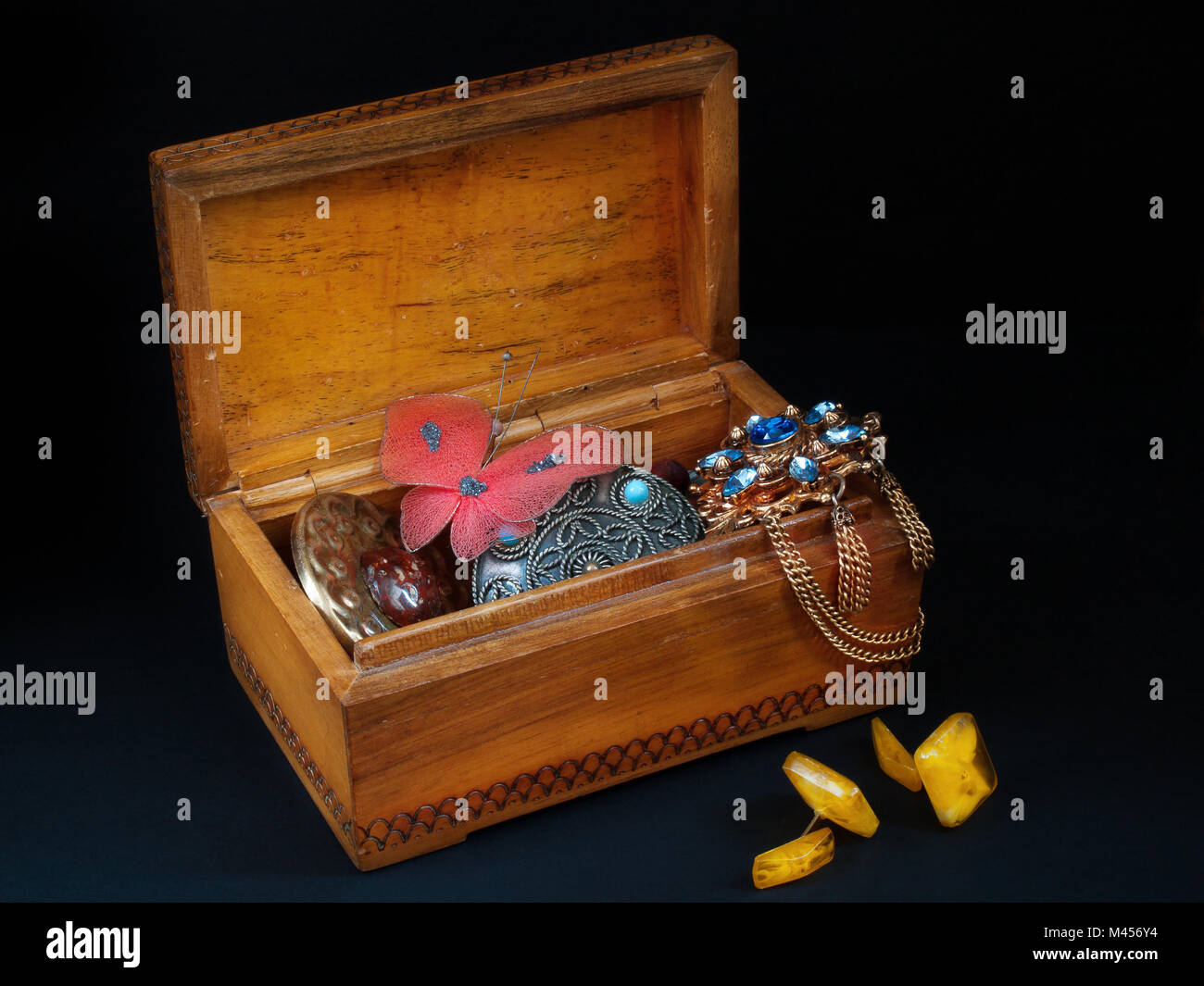 Aprire un vecchio scrigno di legno con il vecchio rotto decorazioni all'interno e ambra bracciale link vicino a scrigno stand su sfondo nero Foto Stock