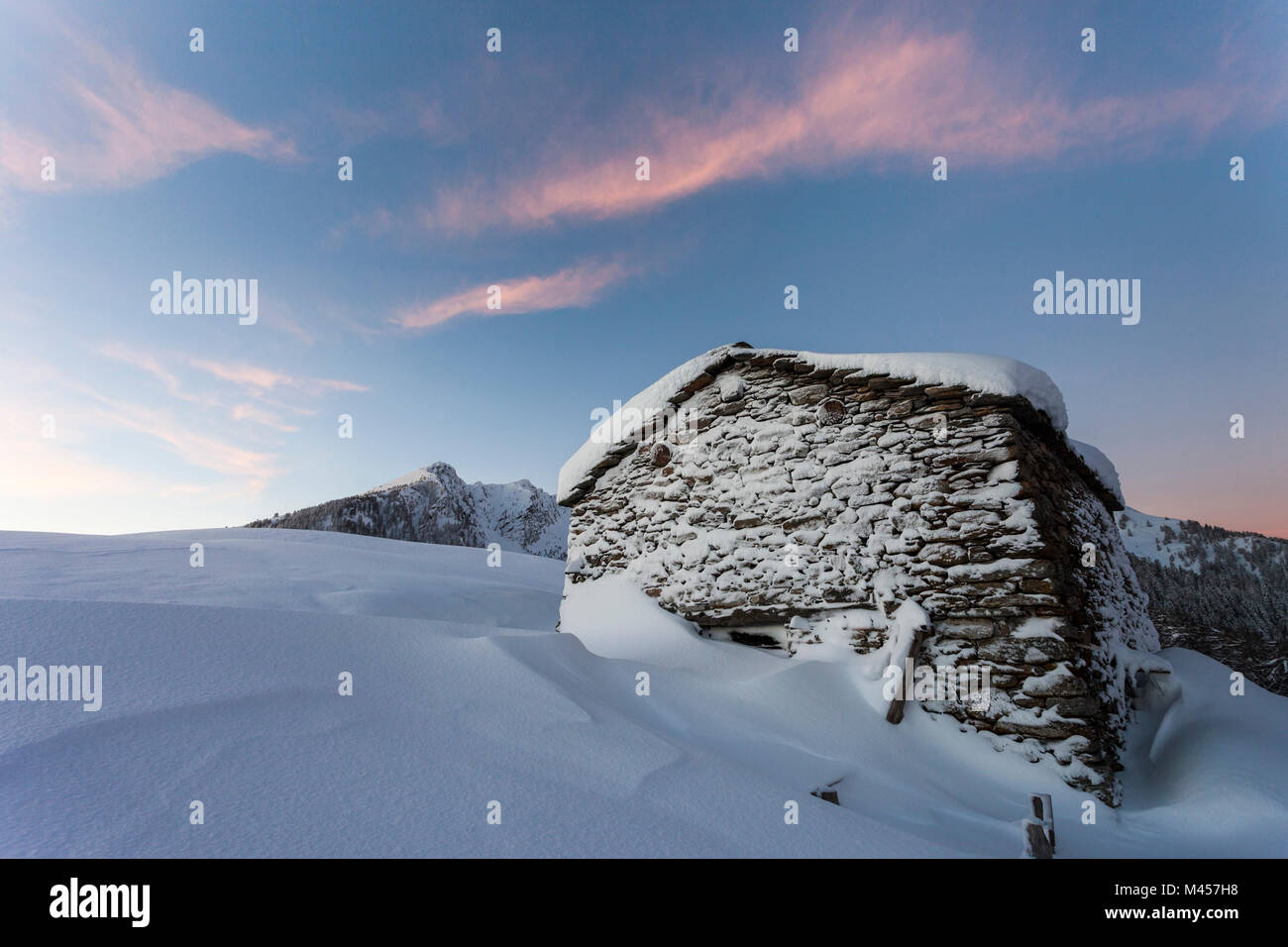 Capanna di pietra ricoperta di neve a sunrise, Monte Olano, Gerola, provincia di Sondrio e della Valtellina, Lombardia, Italia Foto Stock