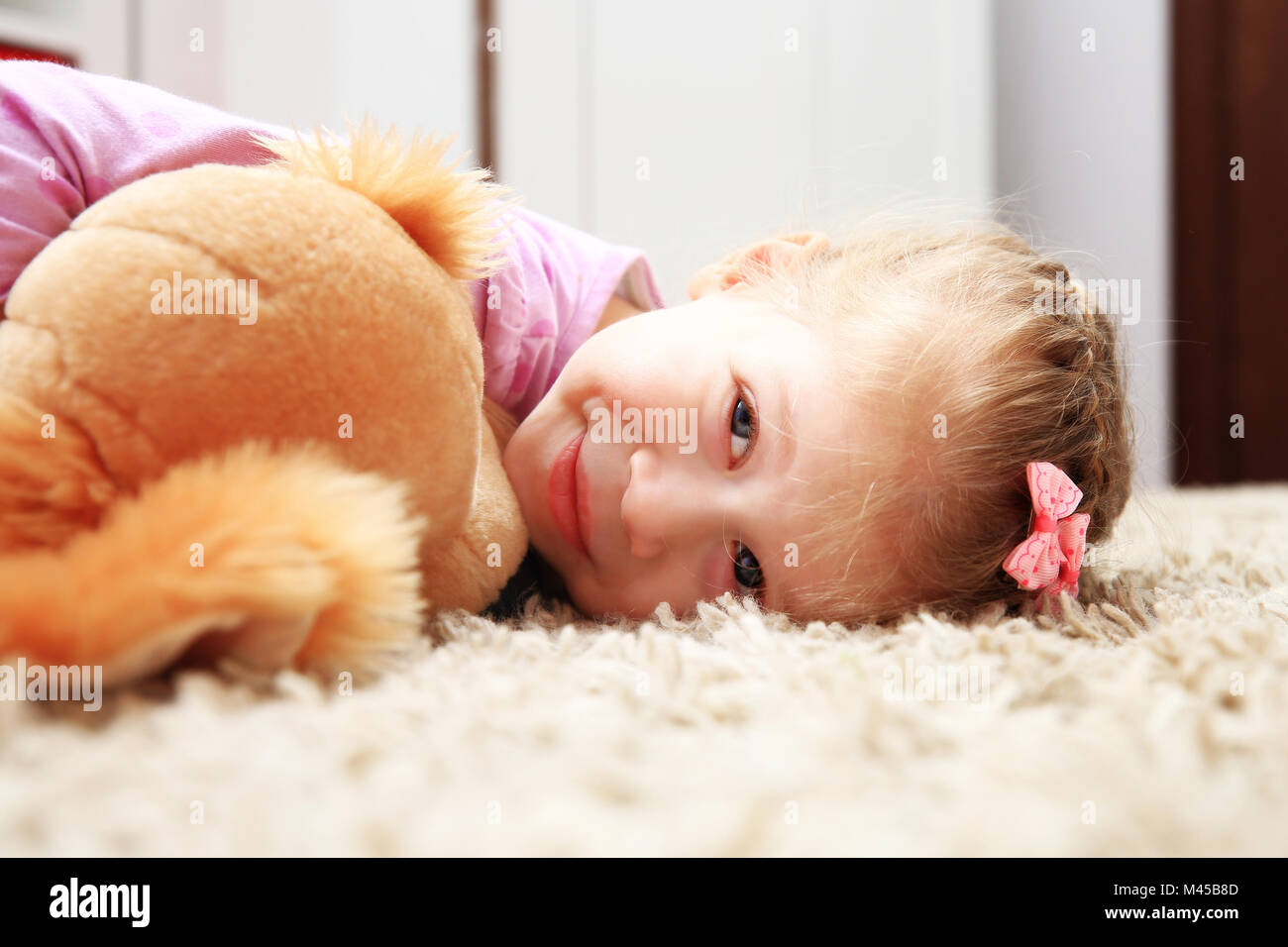 Felice bambina giacente sul soffice tappeto con il suo cane giocattolo. Appoggio per bimbi in camera propria. Foto Stock