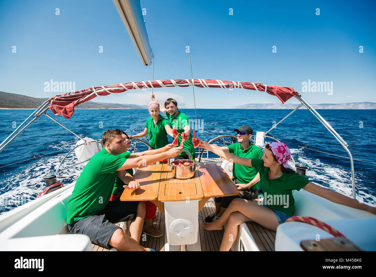 Gli uomini e le giovani donne a bordo di yacht sollevando un brindisi con acqua a fette di melone, Croazia Foto Stock