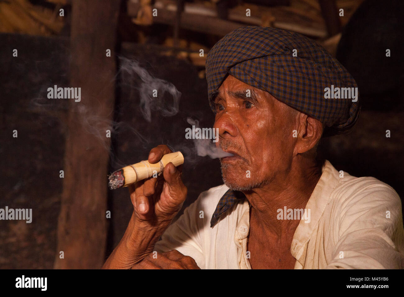 Locale uomo birmano di fumare il sigaro dal fuoco nella sua casa di Bagan Myanmar Foto Stock