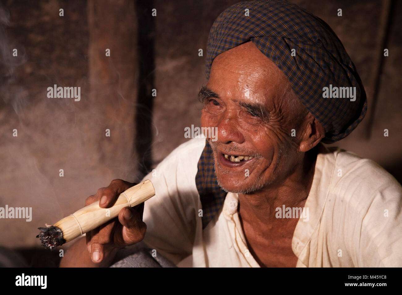 Locale uomo birmano di fumare il sigaro dal fuoco nella sua casa di Bagan Myanmar Foto Stock