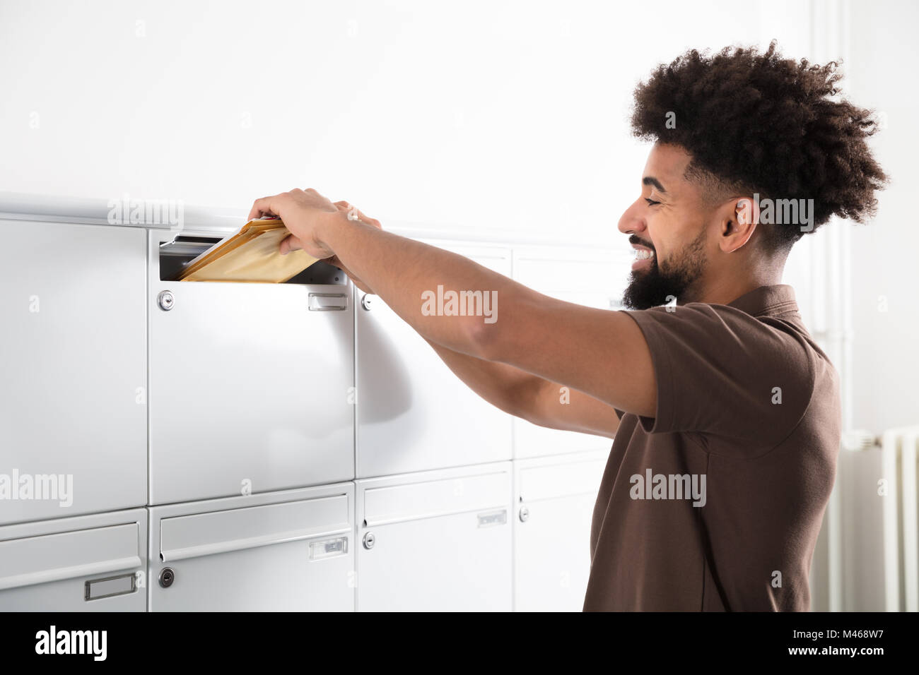 Vista laterale di un giovane uomo di mettere le lettere nella casella di posta Foto Stock