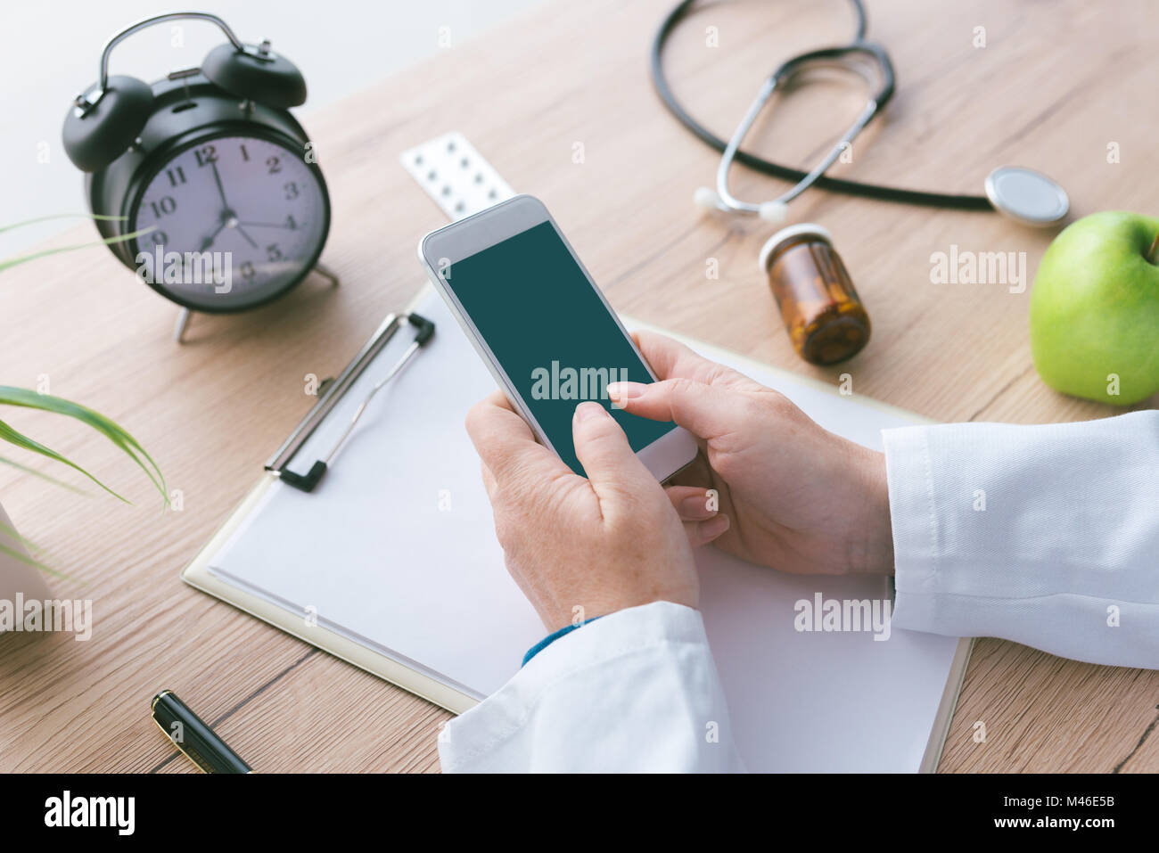 Medico utilizza lo smartphone app in ospedale ufficio, ravvicinata di una persona di sesso femminile mani tenendo il telefono cellulare con schermo vuoto come mock up copia spazio. Moderno t Foto Stock