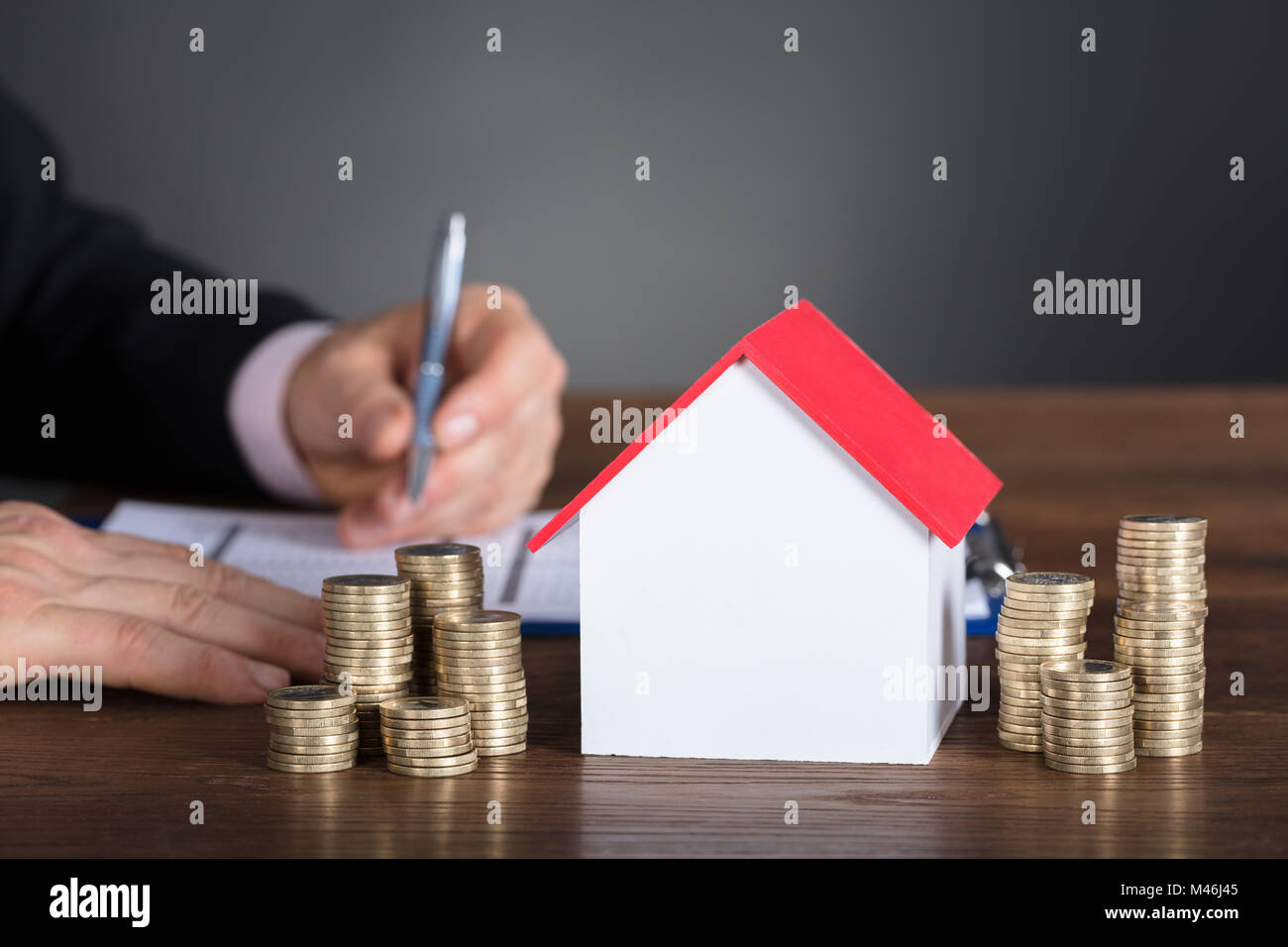 Imprenditore calcolo delle imposte dal modello di casa e pile di monete sul tavolo Foto Stock