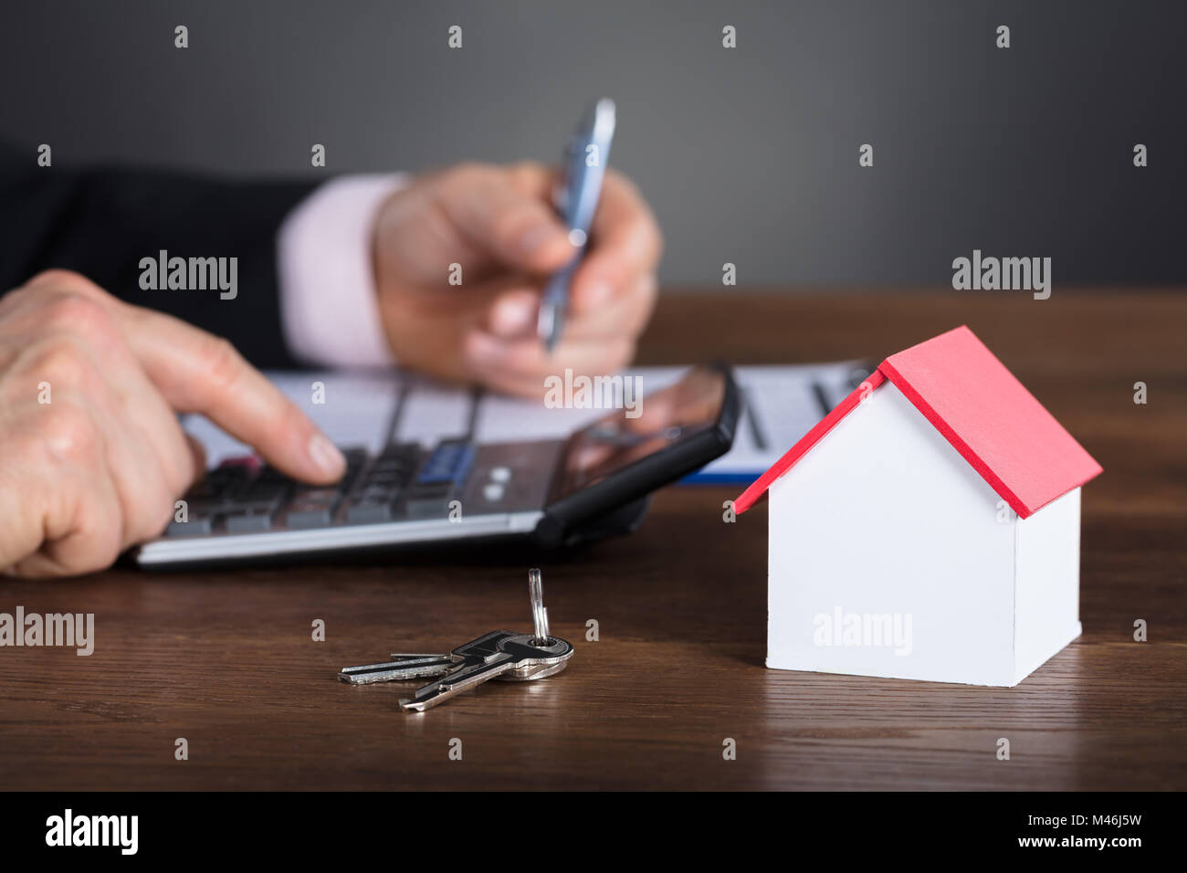 Imprenditore Casa di calcolo dei costi con calcolatrice con modello di casa e la chiave sulla scrivania in legno Foto Stock