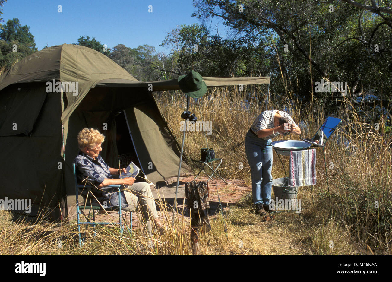 Lo Zimbabwe. Vicino a Victoria Falls. Fiume Zambesi. Il turista. Camping. Donna di fronte a tenda di lettura e di lavaggio. Foto Stock