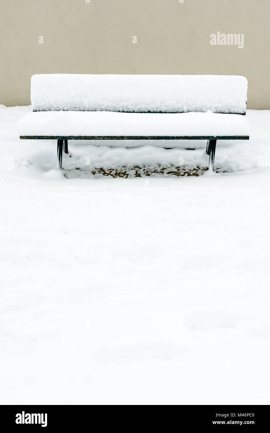 Vista frontale di un pubblico panca in legno ricoperta di neve di fronte a un muro nel giardino del Trocadero a Parigi. Foto Stock