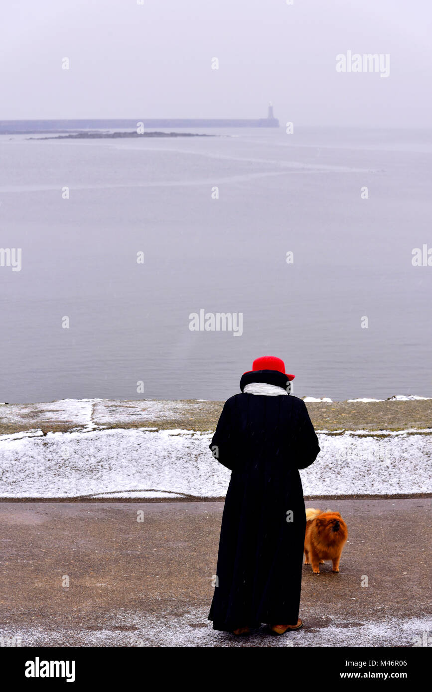 Signora dog walker nella neve a North Shields guardando verso di Tynemouth Foto Stock